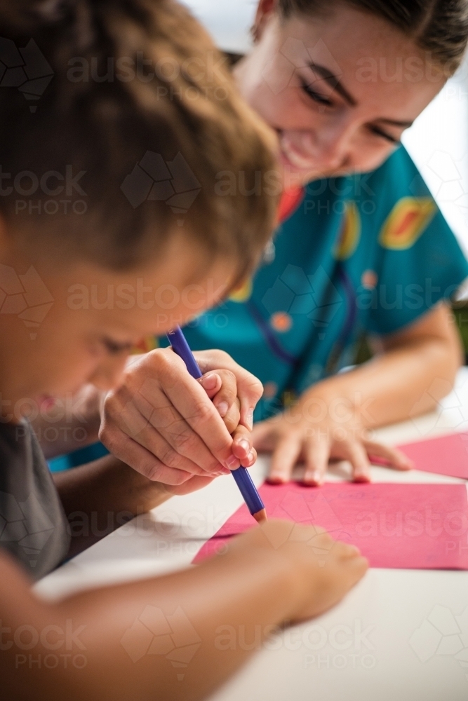 Young Aboriginal boy writing with teacher - Australian Stock Image