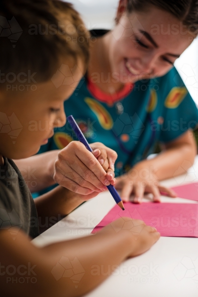 Young Aboriginal boy writing with teacher - Australian Stock Image