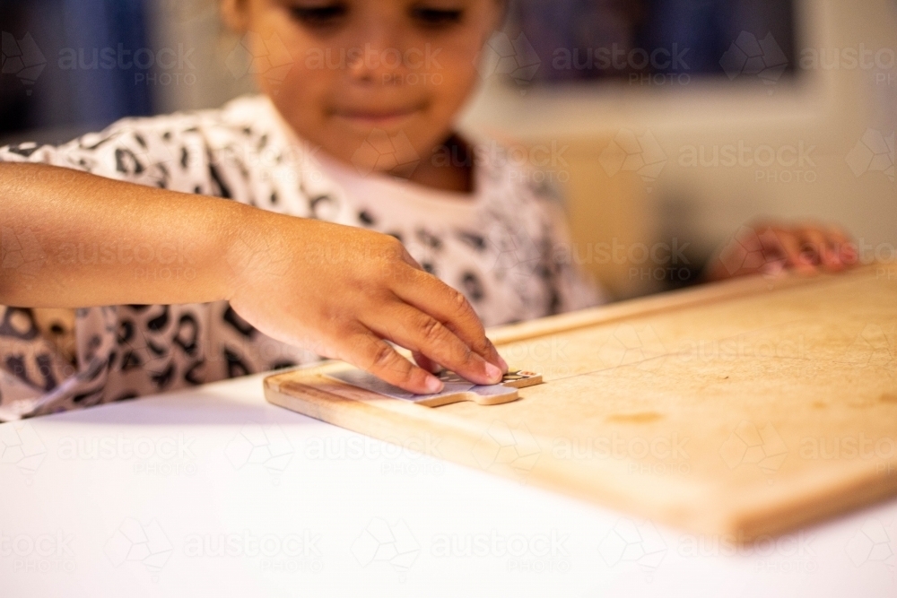 Young Aboriginal girl at preschool doing a puzzle with a teacher - Australian Stock Image