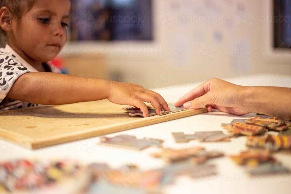 Young Aboriginal girl at preschool doing a puzzle with a teacher - Australian Stock Image