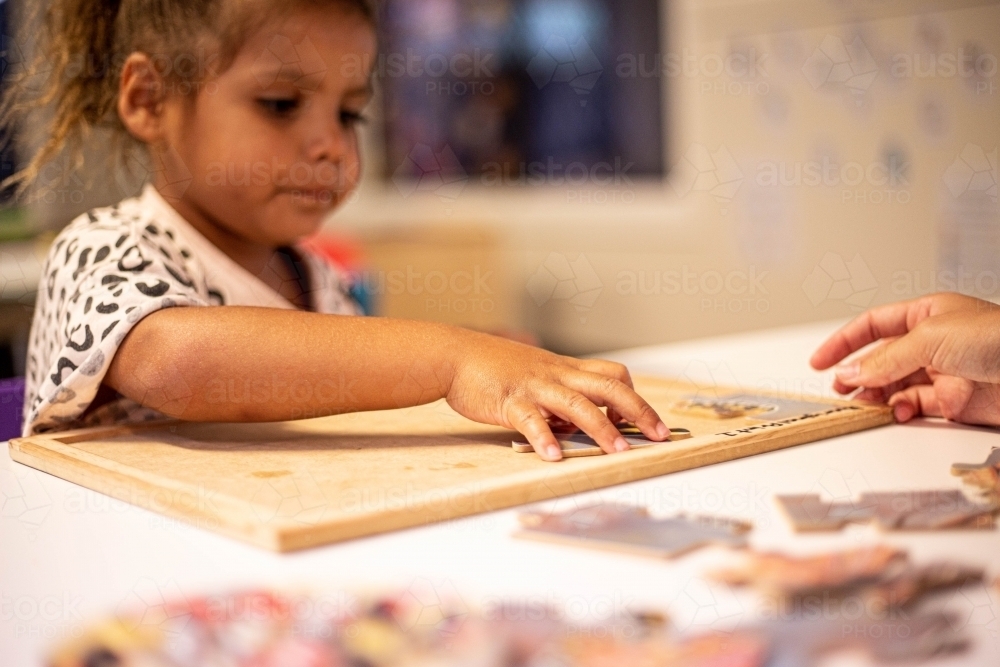 Young Aboriginal girl at preschool doing a puzzle with a teacher - Australian Stock Image