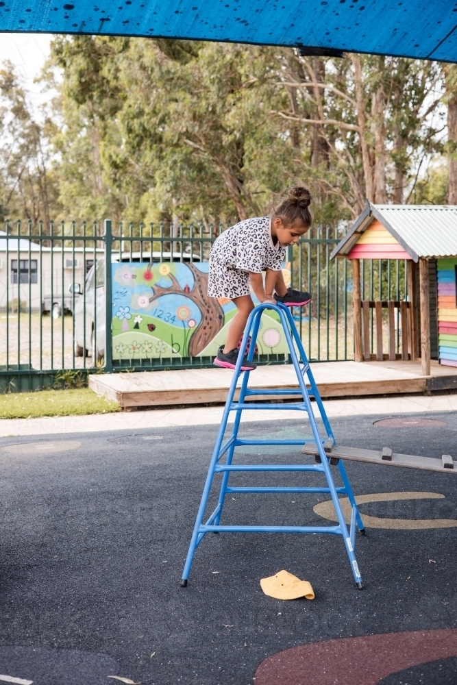 Young Aboriginal girl climbing over a ladder at preschool - Australian Stock Image