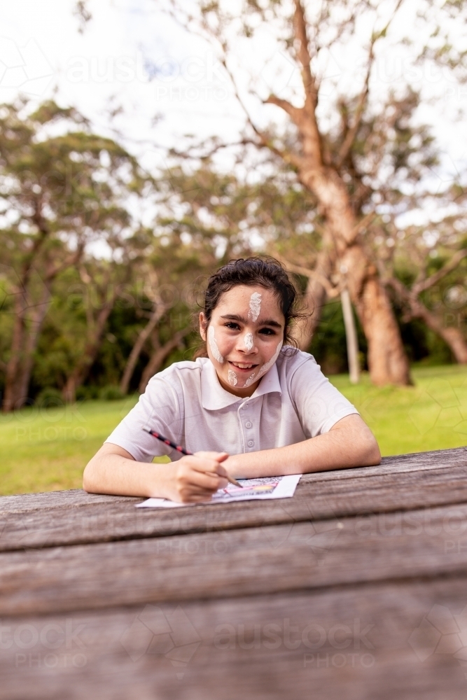 Young Aboriginal girl drawing at a table and smiling at the camera - Australian Stock Image