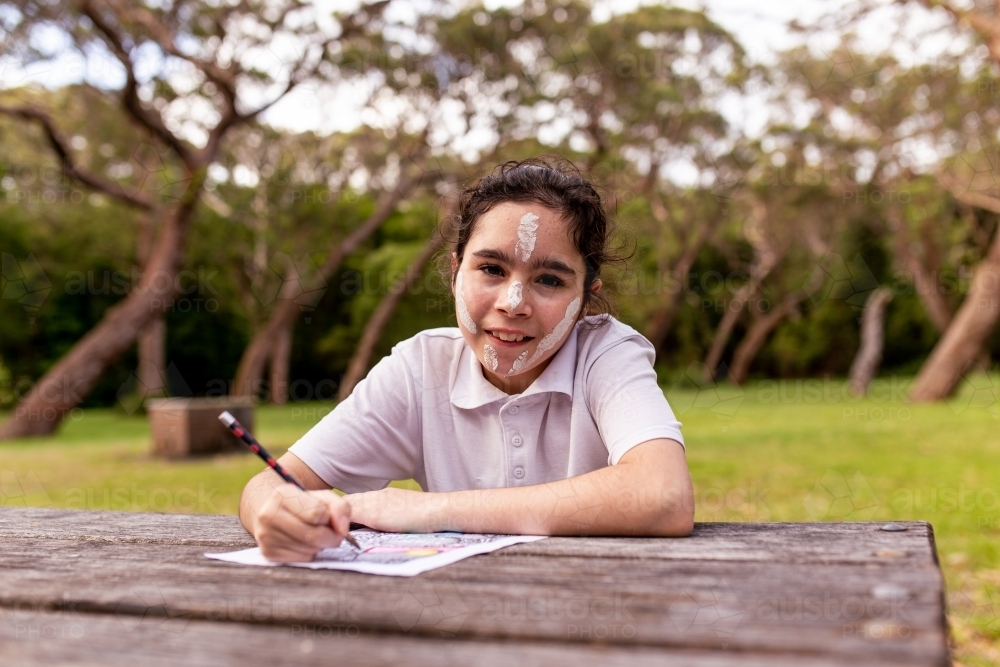 Young Aboriginal girl sitting and drawing at an outdoor table - Australian Stock Image