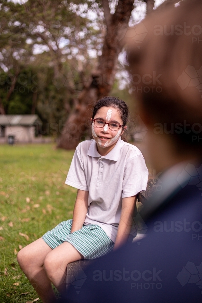 Young Aboriginal girl wearing white face paint and glasses smiling at the camera - Australian Stock Image