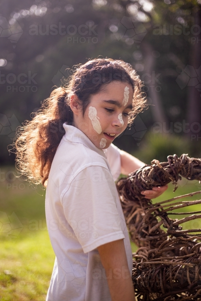 Young Aboriginal girl wearing white face paint holding a wooden basket - Australian Stock Image