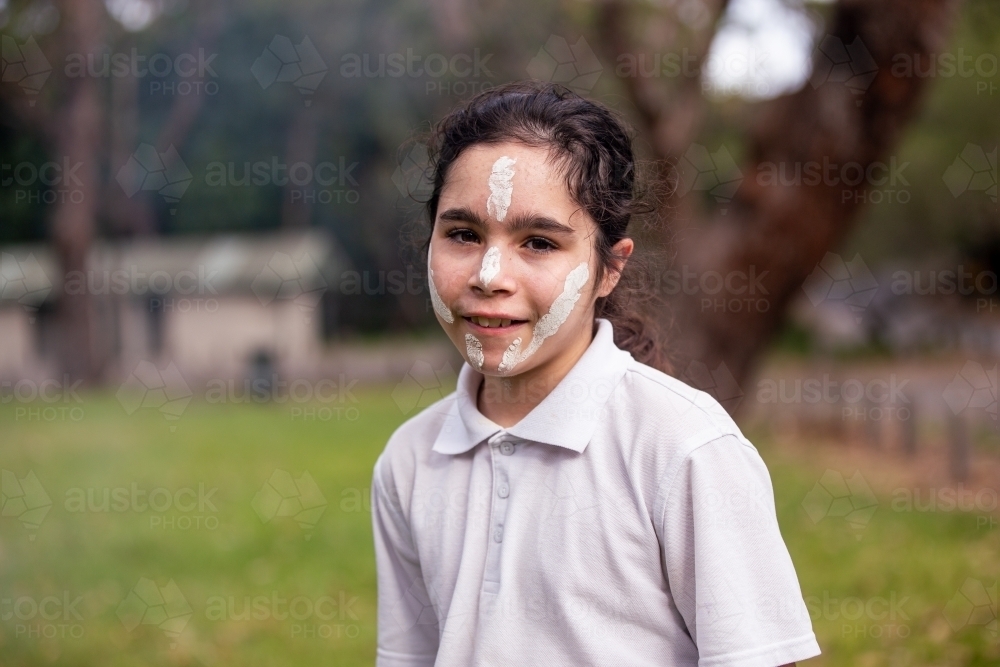 Young Aboriginal girl wearing white face paint smiling at the camera - Australian Stock Image