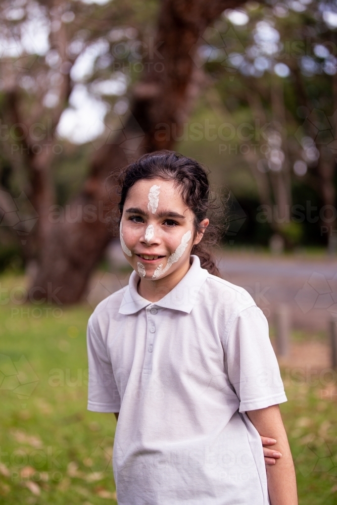 Young Aboriginal girl wearing white face paint smiling at the camera - Australian Stock Image