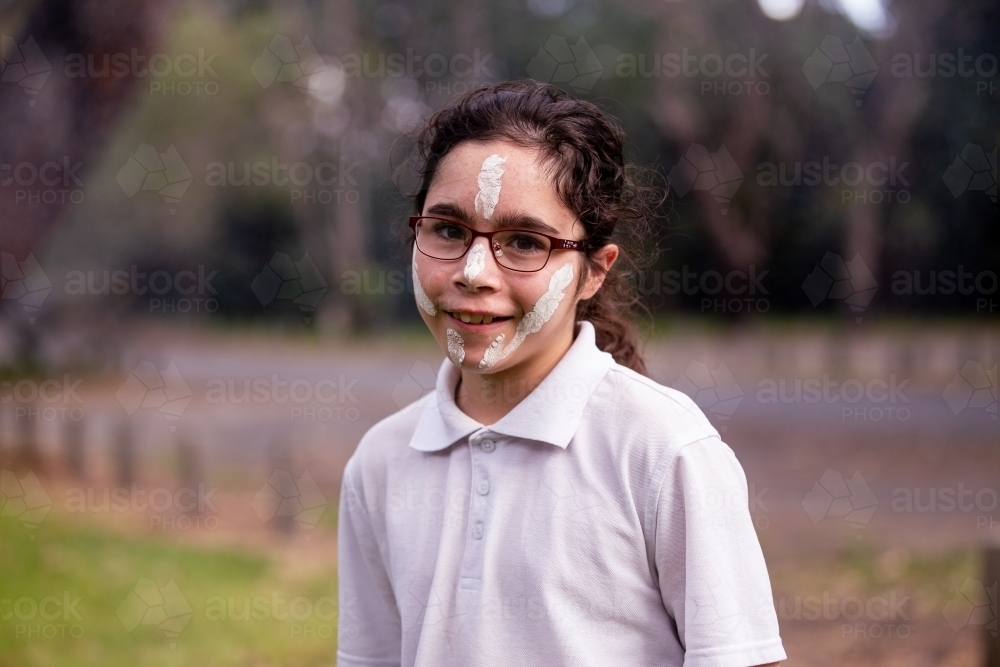 Young Aboriginal girl wearing white face paint smiling at the camera - Australian Stock Image