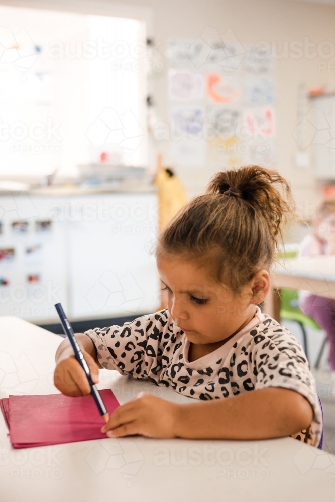 Young Aboriginal girl writing at preschool - Australian Stock Image