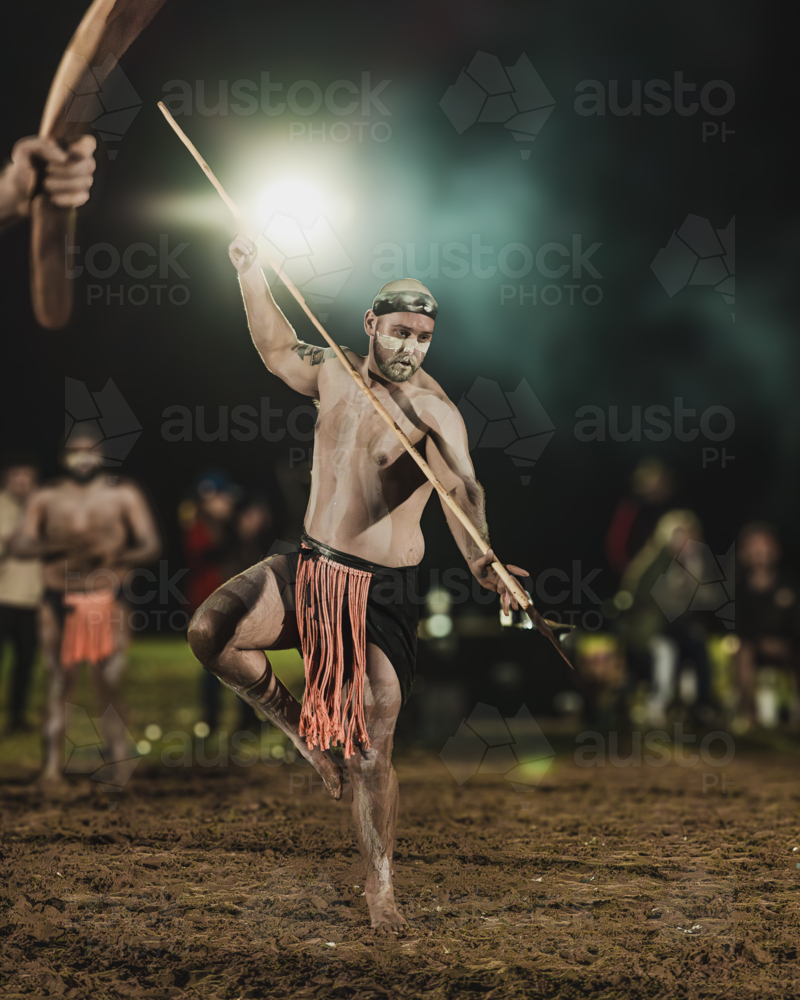 Young Aboriginal Male dancing during a night Corroboree with a spear - Australian Stock Image