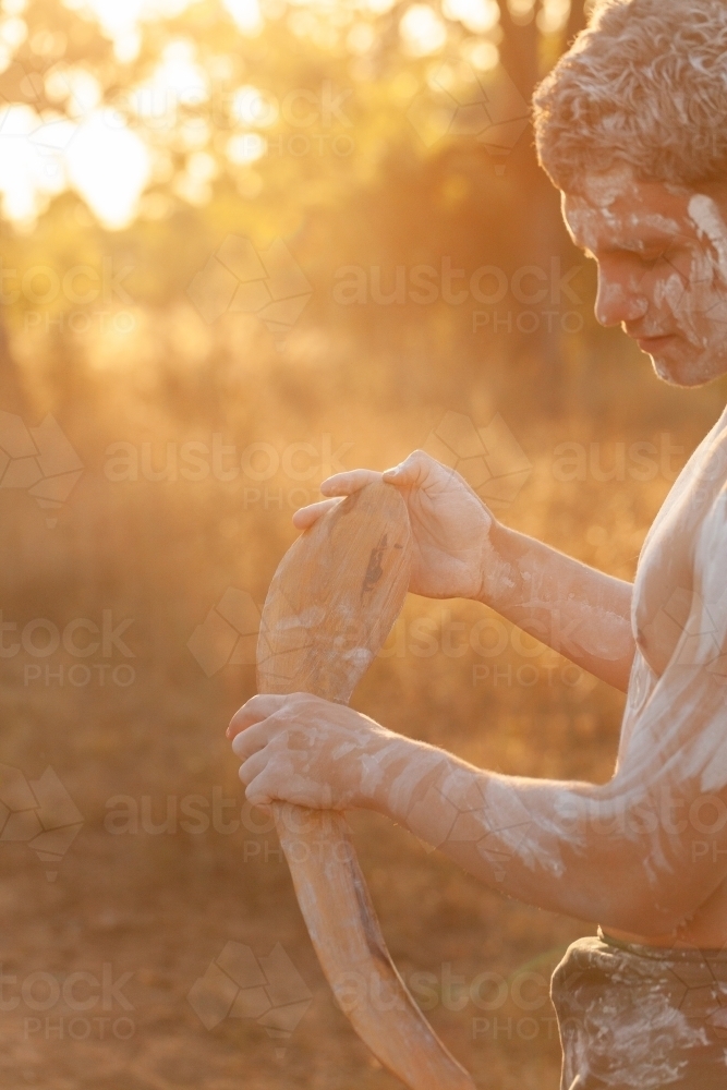 Young Aboriginal  man holding digging stick in golden sunlight - Australian Stock Image