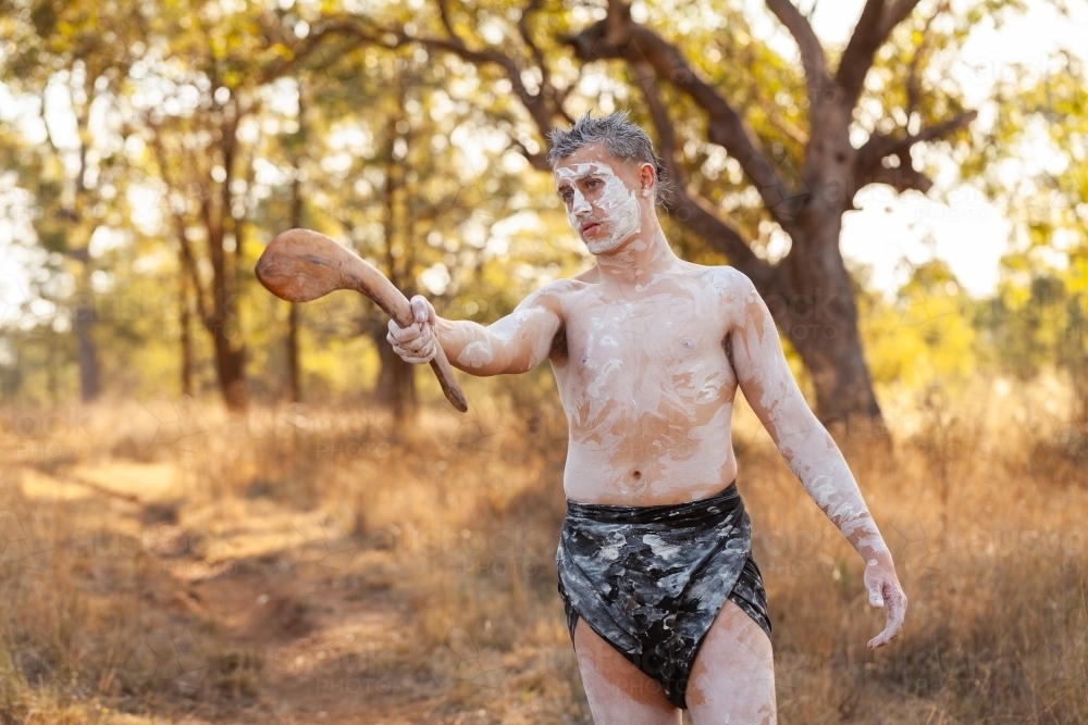 Young aboriginal man pointing with traditional stick in bushland telling stories of Australia - Australian Stock Image