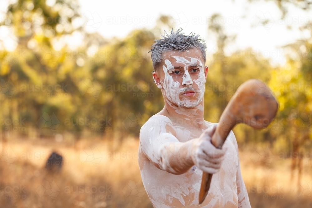 Young aboriginal man pointing with traditional stick in bushland telling stories of Australia - Australian Stock Image