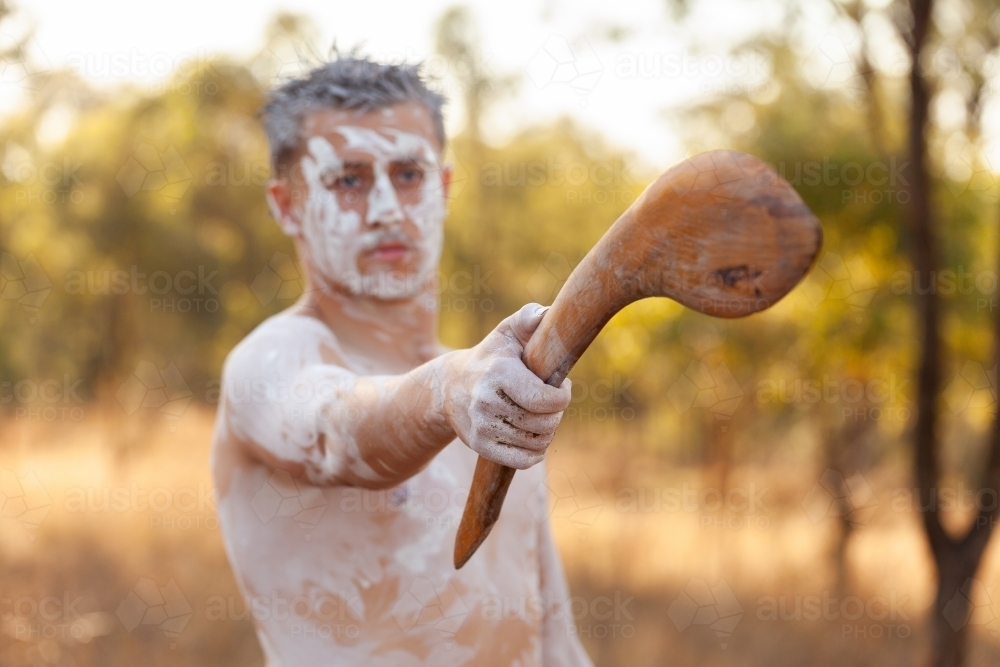 Young aboriginal man pointing with traditional stick in bushland telling stories of Australia - Australian Stock Image