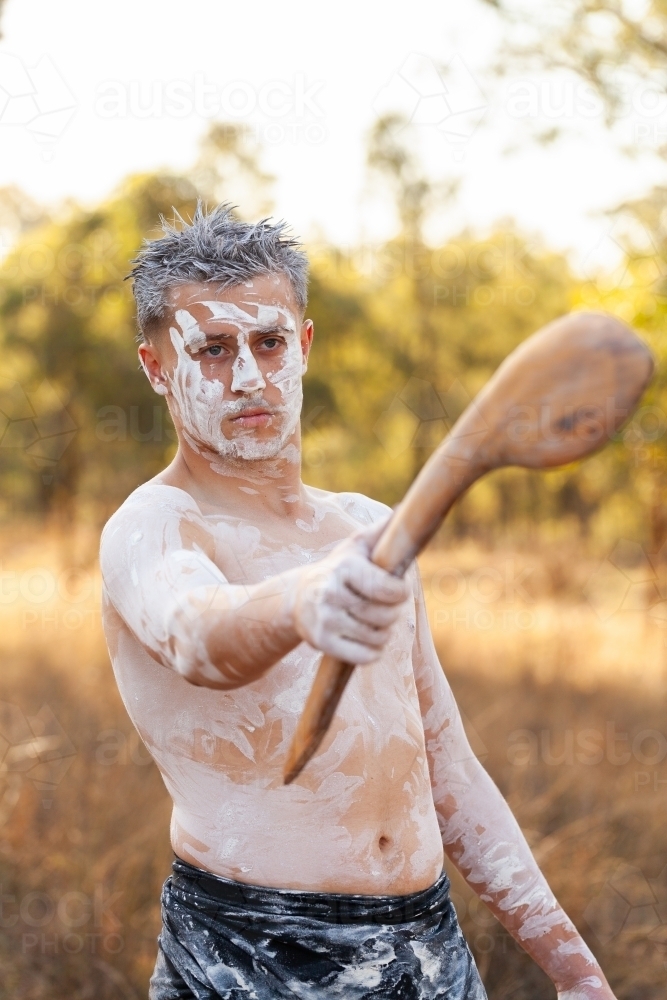 Young aboriginal man pointing with traditional stick in bushland telling stories of Australia - Australian Stock Image