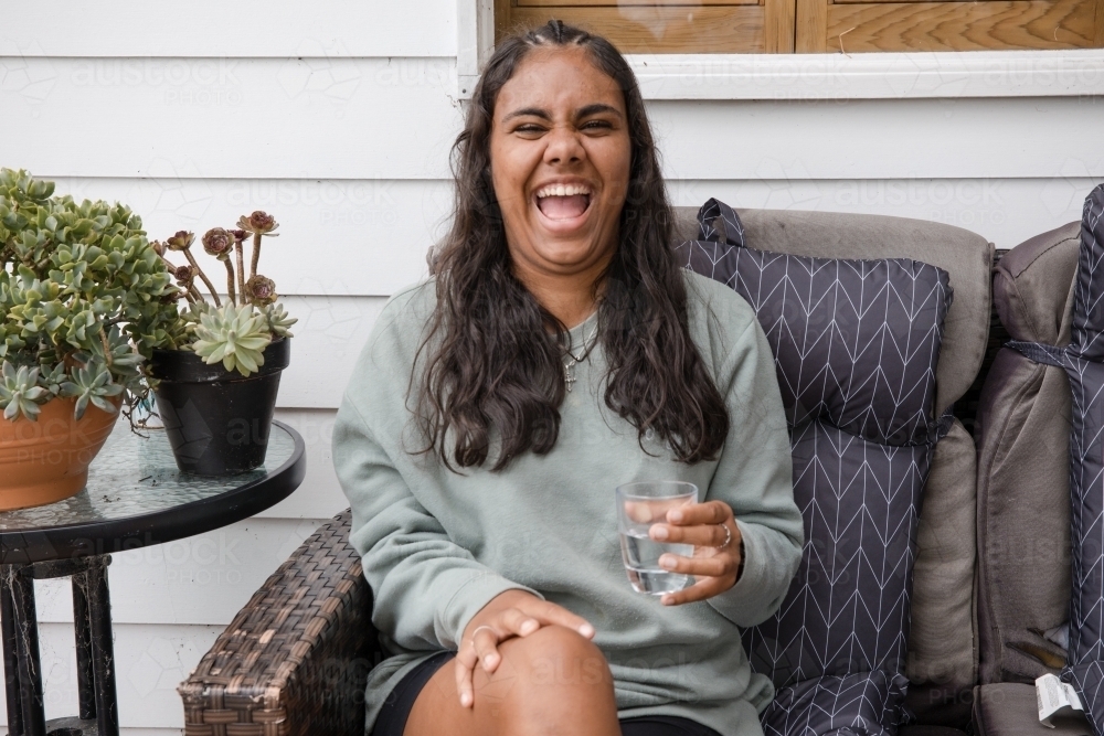 Young Aboriginal woman sitting on a couch outside laughing - Australian Stock Image