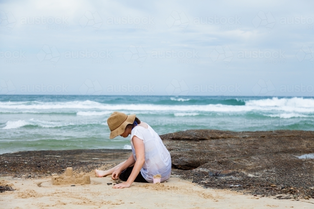 Young adult person building a sandcastle at the beach - Australian Stock Image