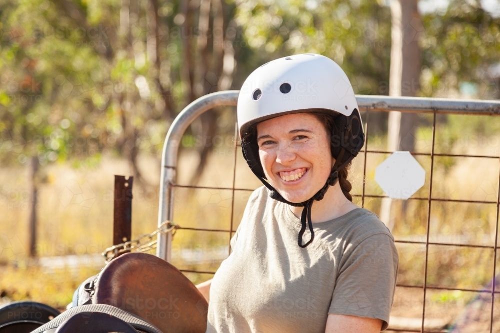 Young adult person in her twenties carrying horses saddle - Australian Stock Image