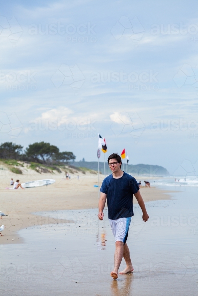 Young adult walking along beach in summer - Australian Stock Image