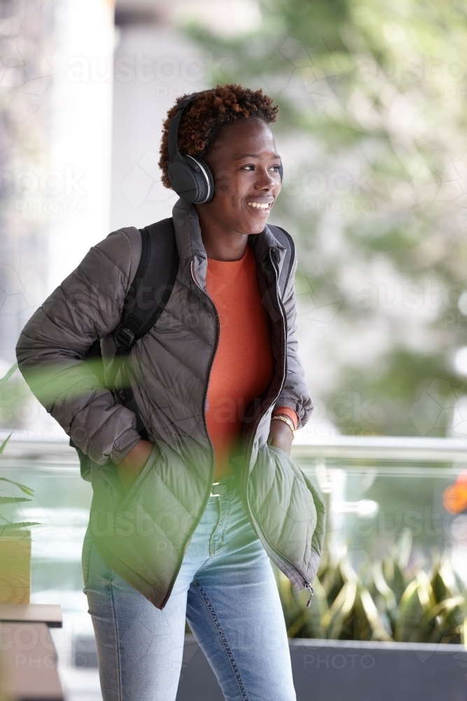 Young African woman listening to music wearing wireless headphones in city - Australian Stock Image