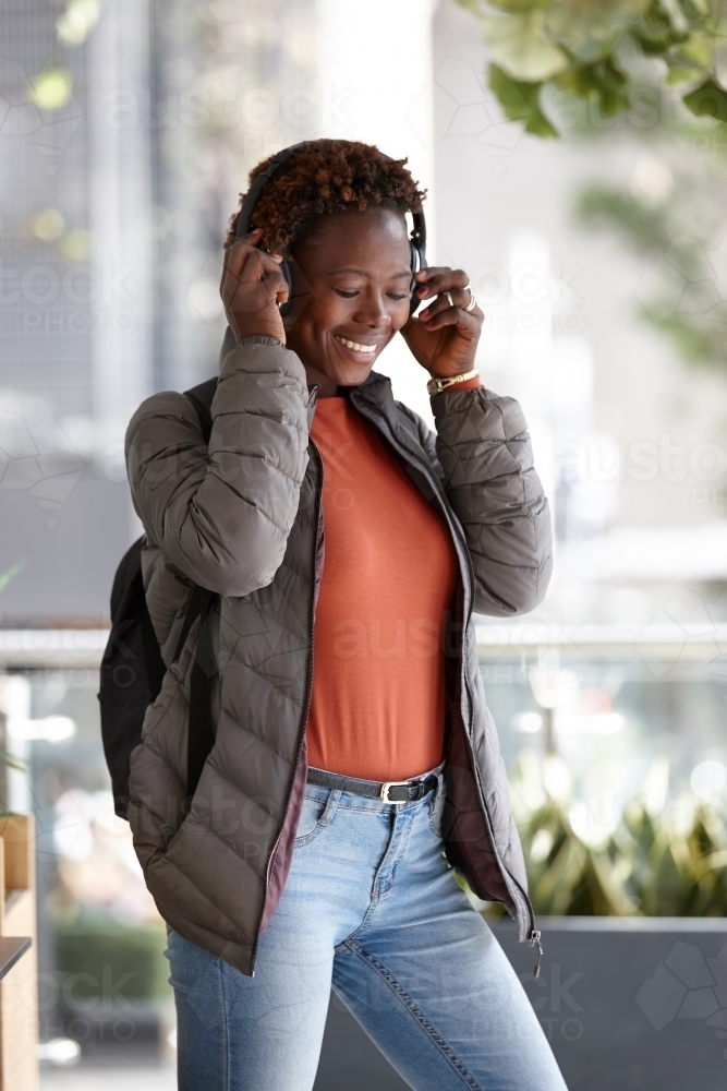 Young African woman listening to music wearing wireless headphones in city - Australian Stock Image