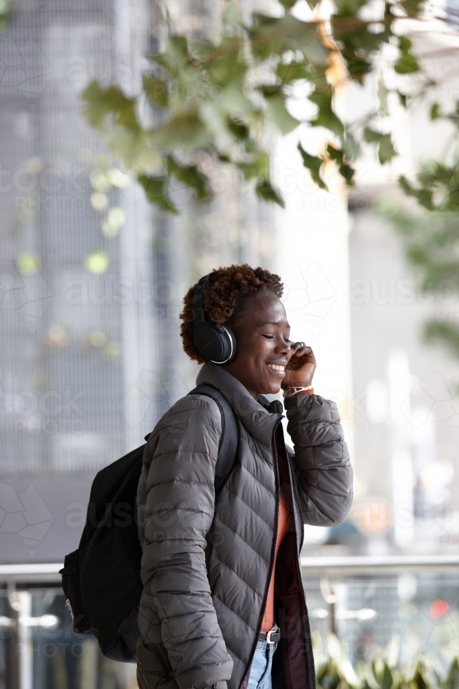 Young African woman listening to music wearing wireless headphones in city - Australian Stock Image