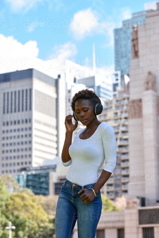 Young African woman listening to music wearing wireless headphones in city - Australian Stock Image