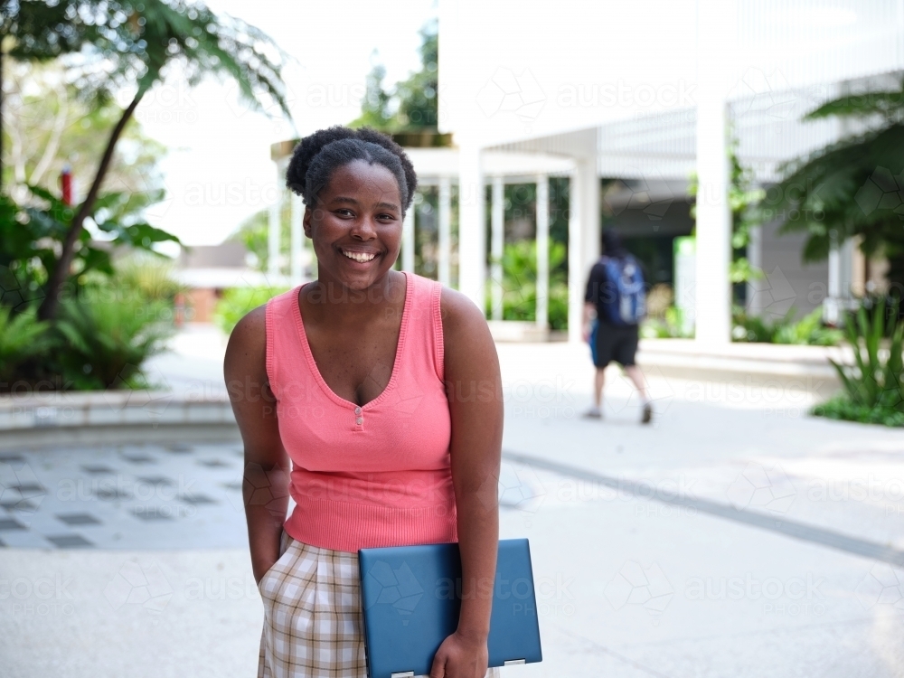 Young African woman standing with laptop in university courtyard - Australian Stock Image