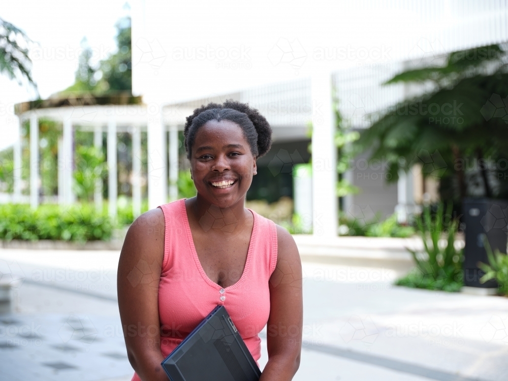 Young African woman standing with laptop in university courtyard - Australian Stock Image