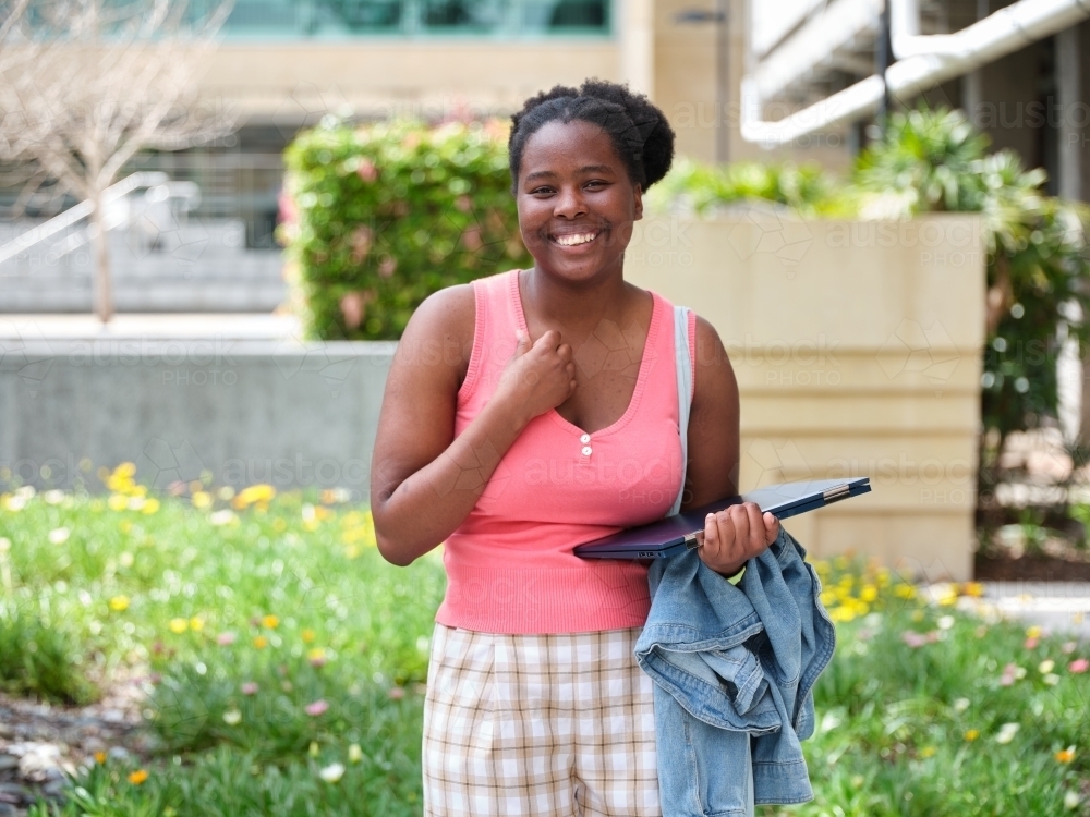 Young African woman standing with laptop in university courtyard - Australian Stock Image