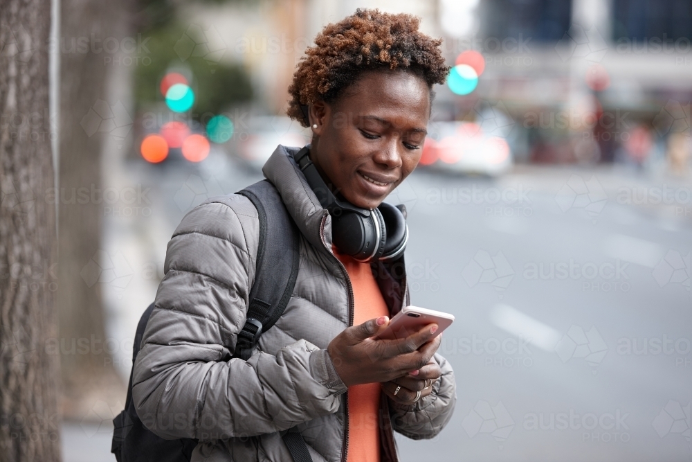 Young African woman text messaging wearing wireless headphones in city - Australian Stock Image