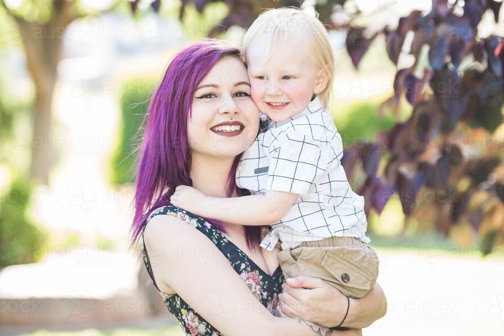 Young alternative mother cuddling young blonde son smiling - Australian Stock Image