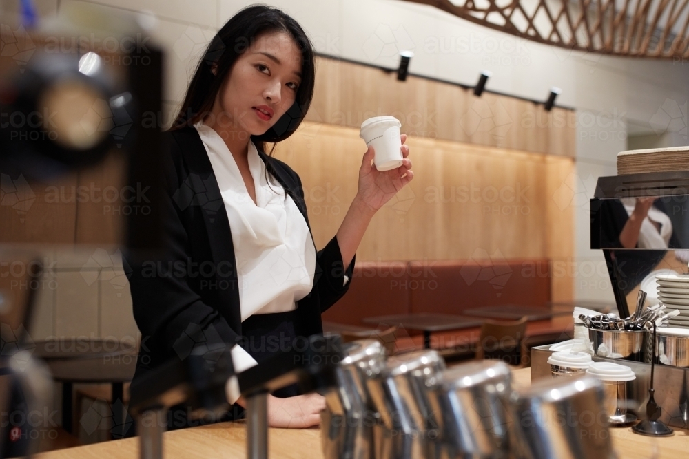 Young Asian business woman drinking coffee and reading newspaper - Australian Stock Image