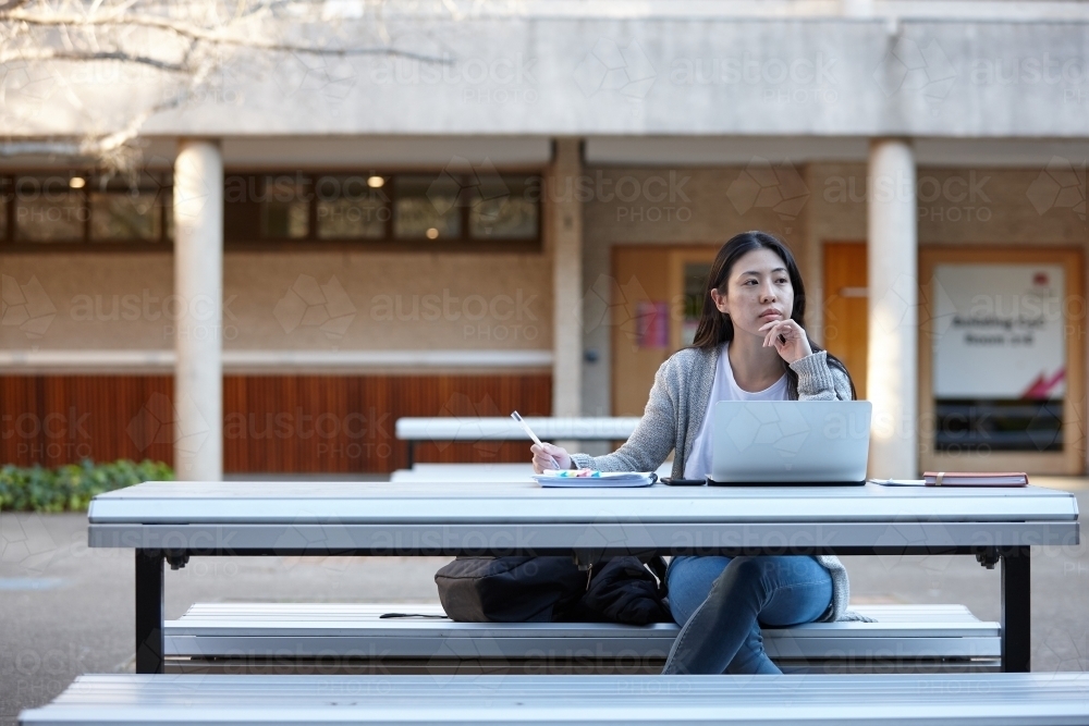 Young Asian female university student studying on laptop outdoors - Australian Stock Image