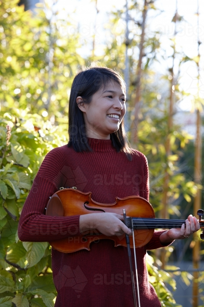 Young Asian female violin player practising outdoors - Australian Stock Image