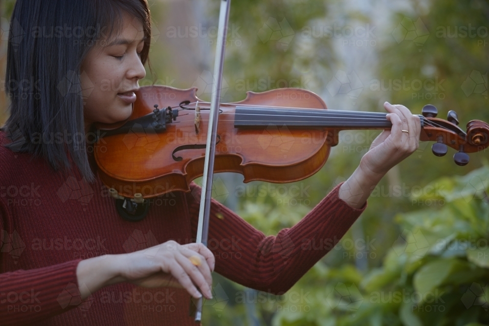 Young Asian female violin player practising outdoors - Australian Stock Image