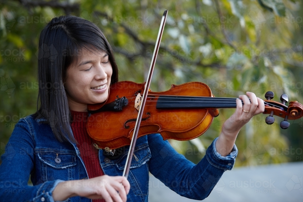 Young Asian female violin player practising outdoors - Australian Stock Image