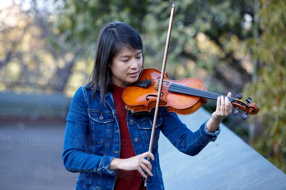 Young Asian female violin player practising outdoors - Australian Stock Image