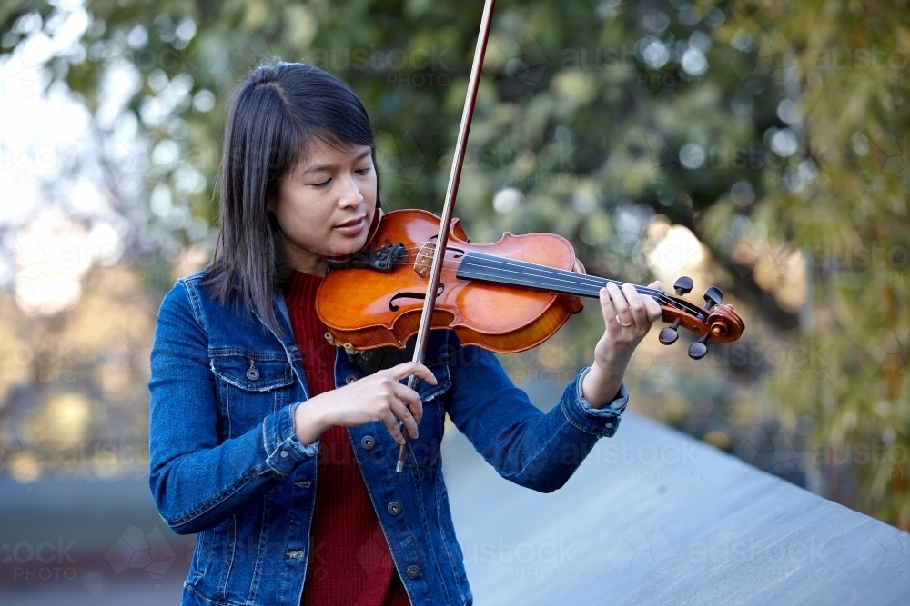 Young Asian female violin player practising outdoors - Australian Stock Image