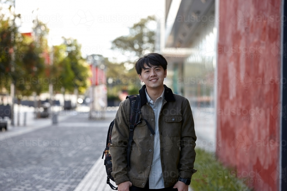 Young Asian student standing outside the university campus - Australian Stock Image