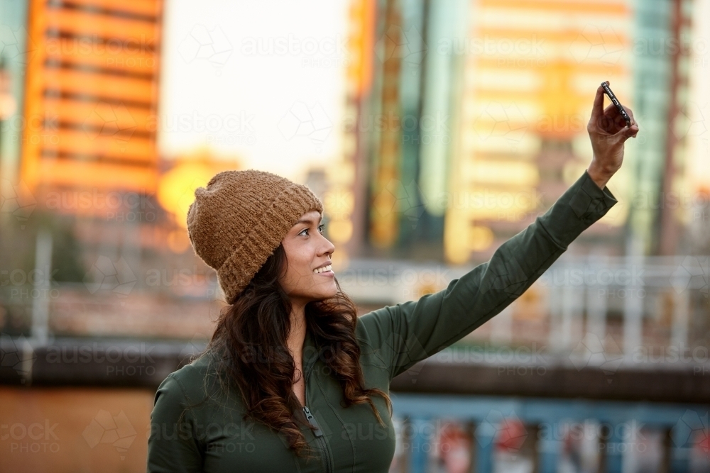 Young Asian woman taking a selfie with mobile phone in city at dusk - Australian Stock Image