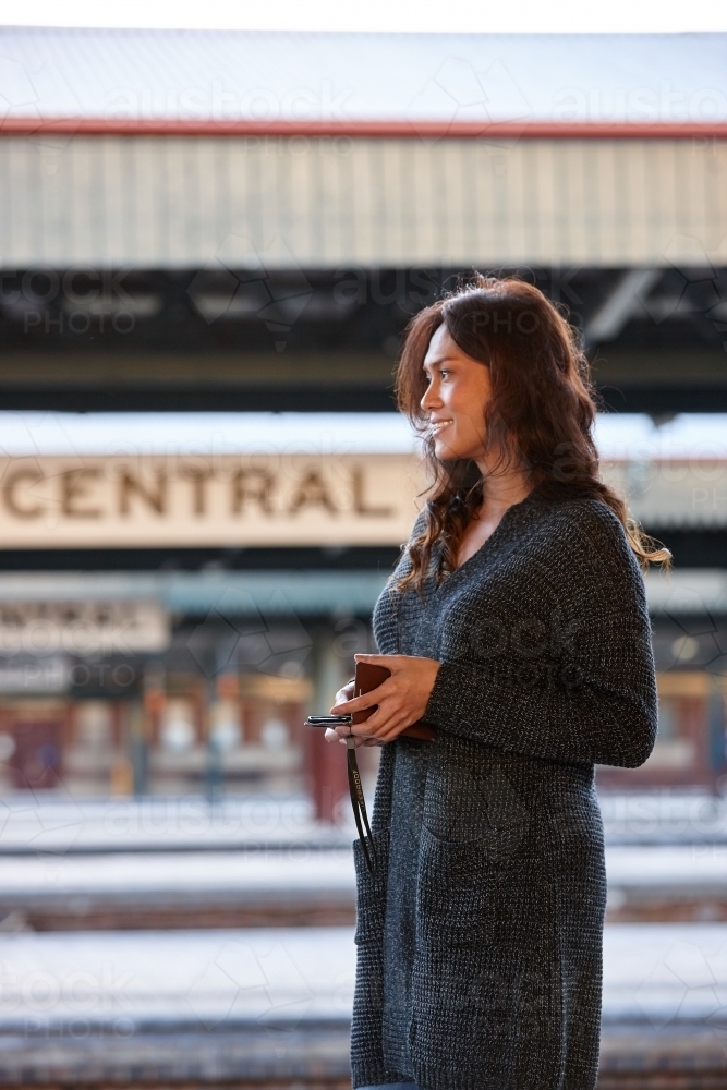 Young Asian woman waiting at train station with mobile phone - Australian Stock Image