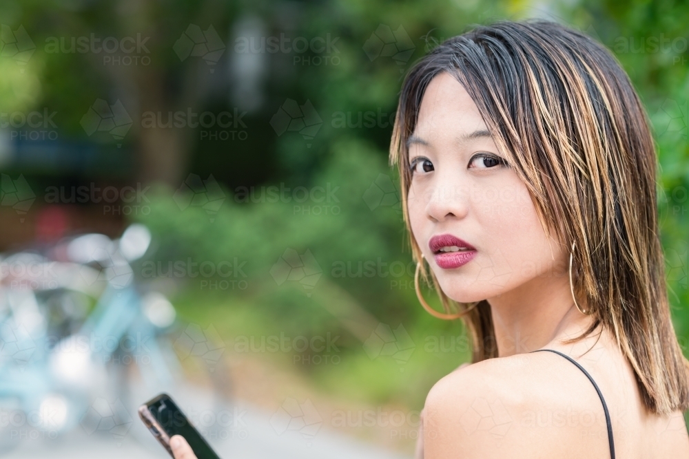 young asian woman with phone looking back at camera - Australian Stock Image