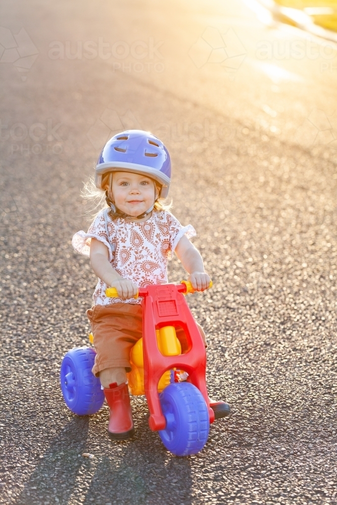 Young Aussie kid riding tricycle dune buggy down quiet suburban road at sunset - Australian Stock Image