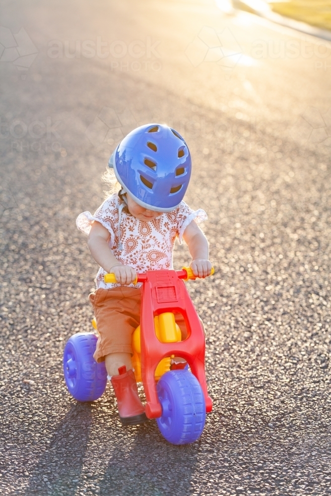 Young Aussie kid riding tricycle dune buggy down quiet suburban road at sunset - Australian Stock Image