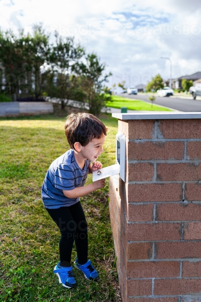 Young Aussie mixed race kid opening mailbox to collect mail - Australian Stock Image