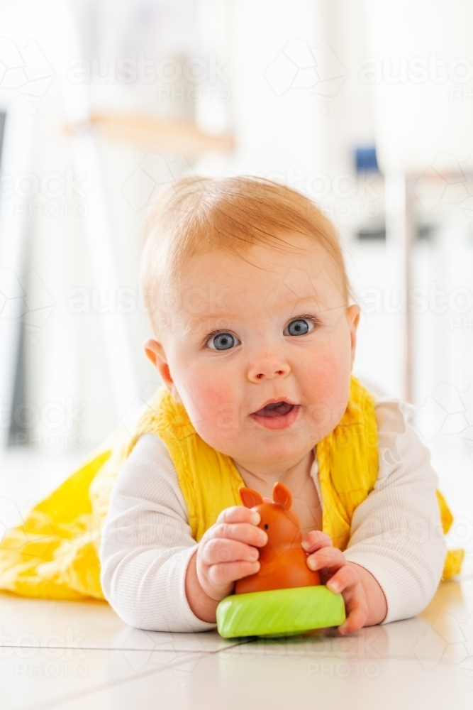 young australian baby girl in yellow dress playing with kangaroo toy on floor - Australian Stock Image