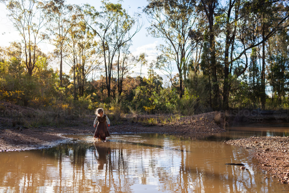 Young Australian child playing beside muddy bushland pool in rural Australia - Australian Stock Image