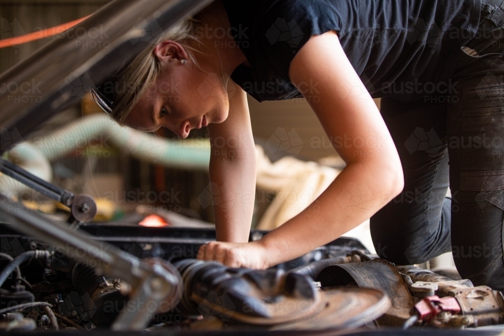 young australian tradesperson mechanic fixing car working under bonnet on engine - Australian Stock Image